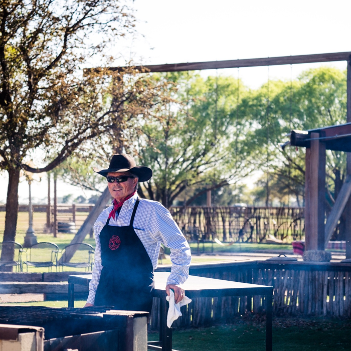 Person grilling outdoors wearing a cowboy hat and apron.
