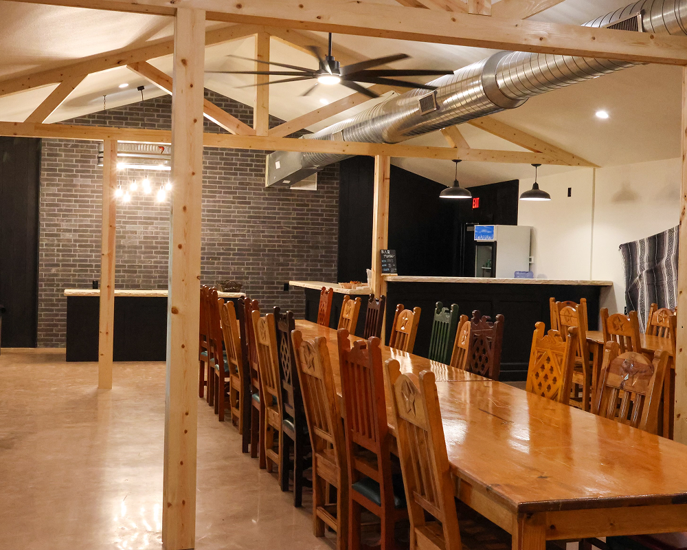 Spacious dining hall with long wooden tables and chairs under exposed wooden beams.