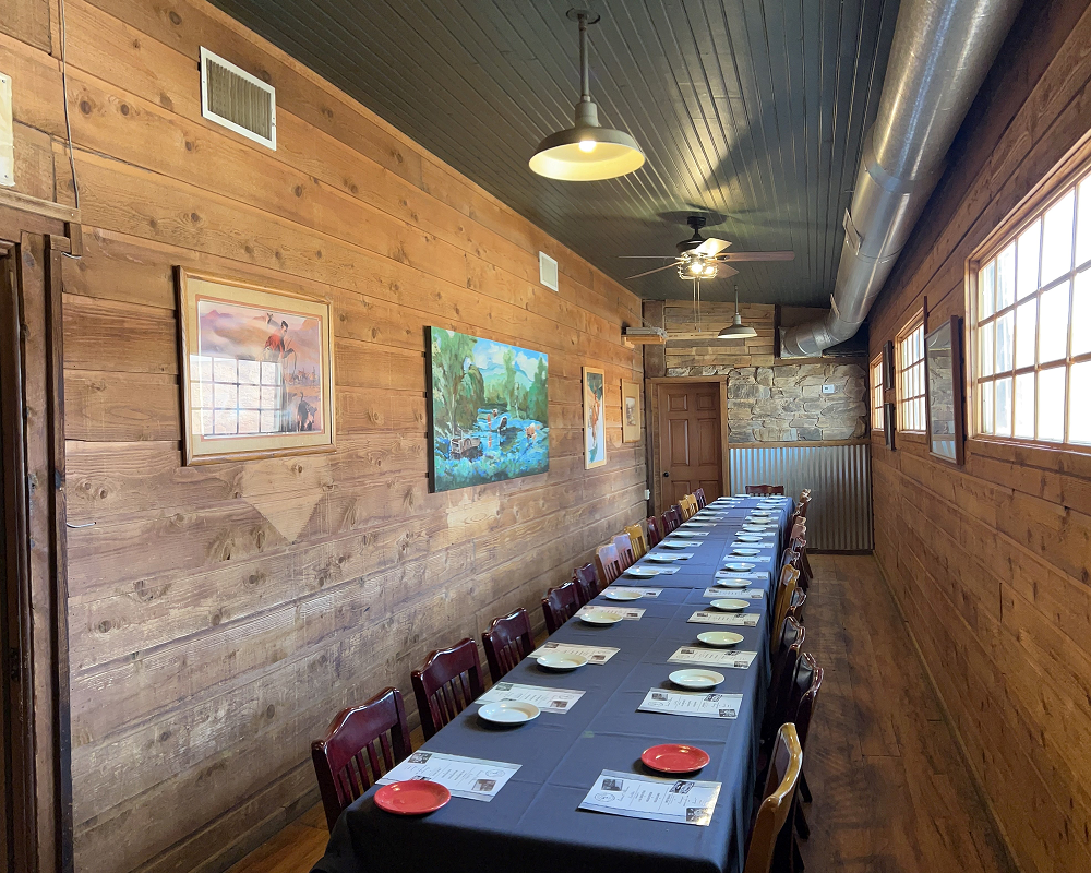 A long dining table set in a rustic room with wooden walls and paintings.