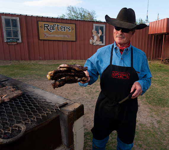 Man in cowboy hat grilling sausages outdoors.