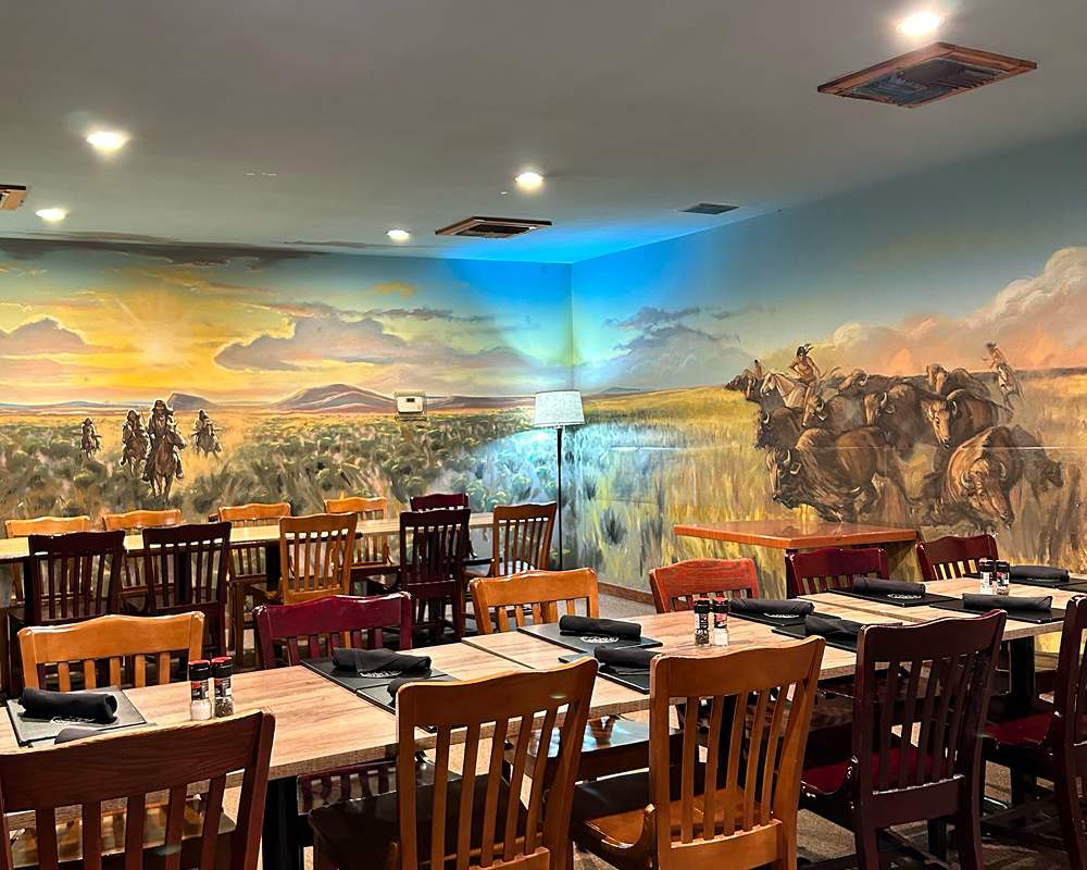 Cozy restaurant interior with wooden chairs and a mural of cowboys on the wall.