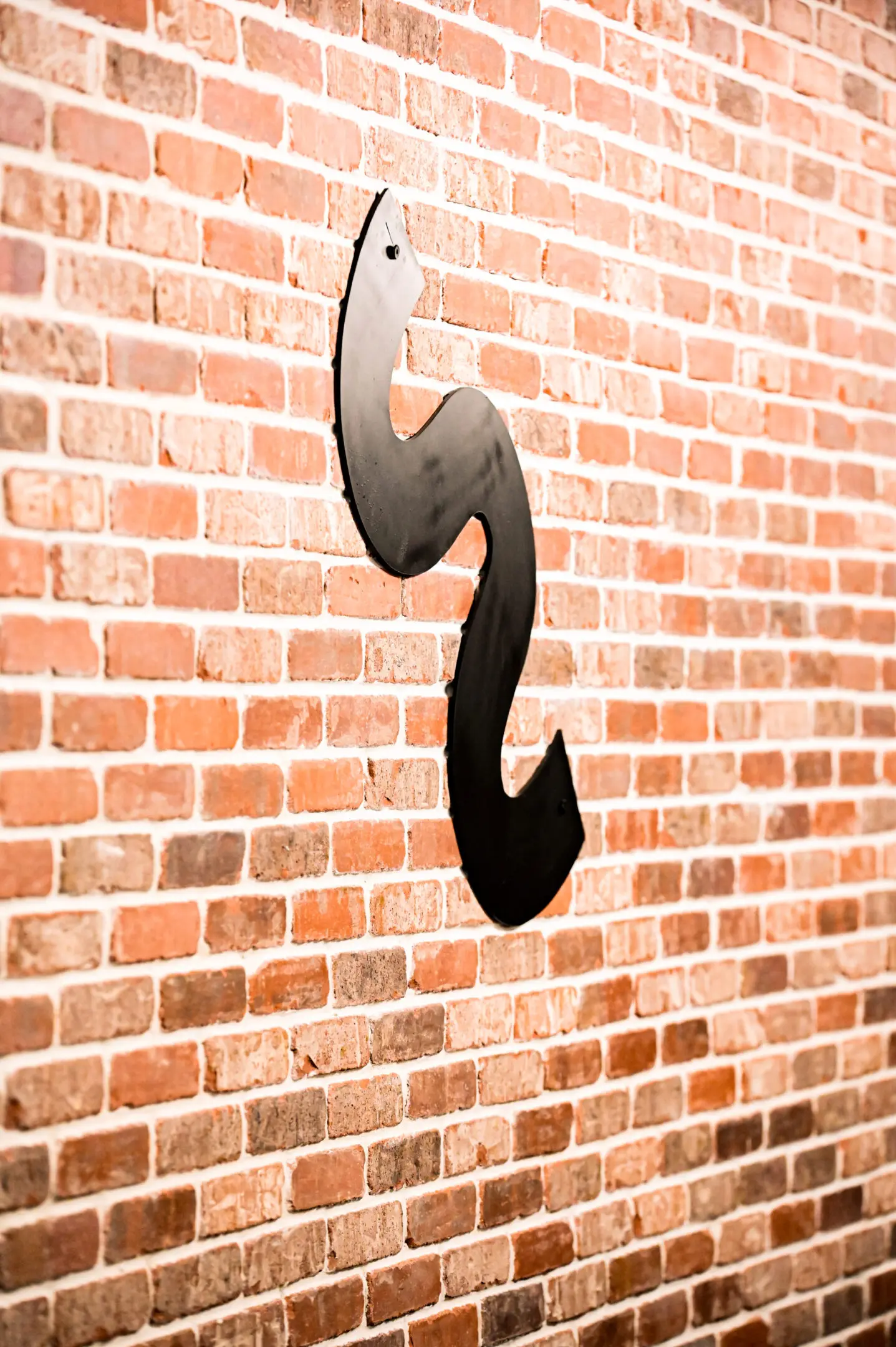 Black metal hook mounted on a brick wall.
