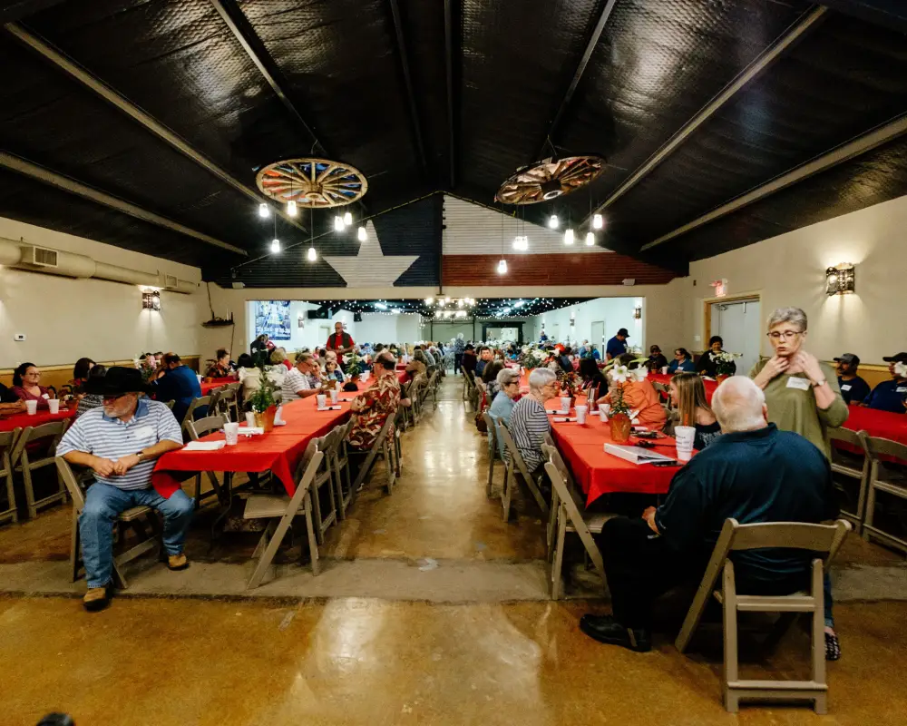 Large group dining in a festive hall with red tablecloths.